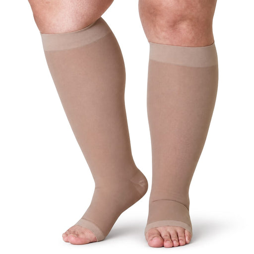 Ben iført beige kompresjonsstrømper for leggene, i pluss-størrelse, mot hvit bakgrunn.