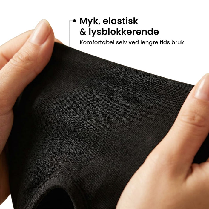 En person som holder en myk, elastisk og lysskjermende svart migrenehatt for å lindre symptomene.