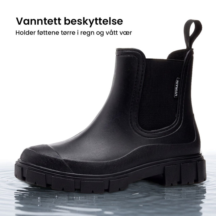 Svarte, vanntette Urban Nordic-støvler med elastisk sidepanel og solid såle, stående i grunt vann.